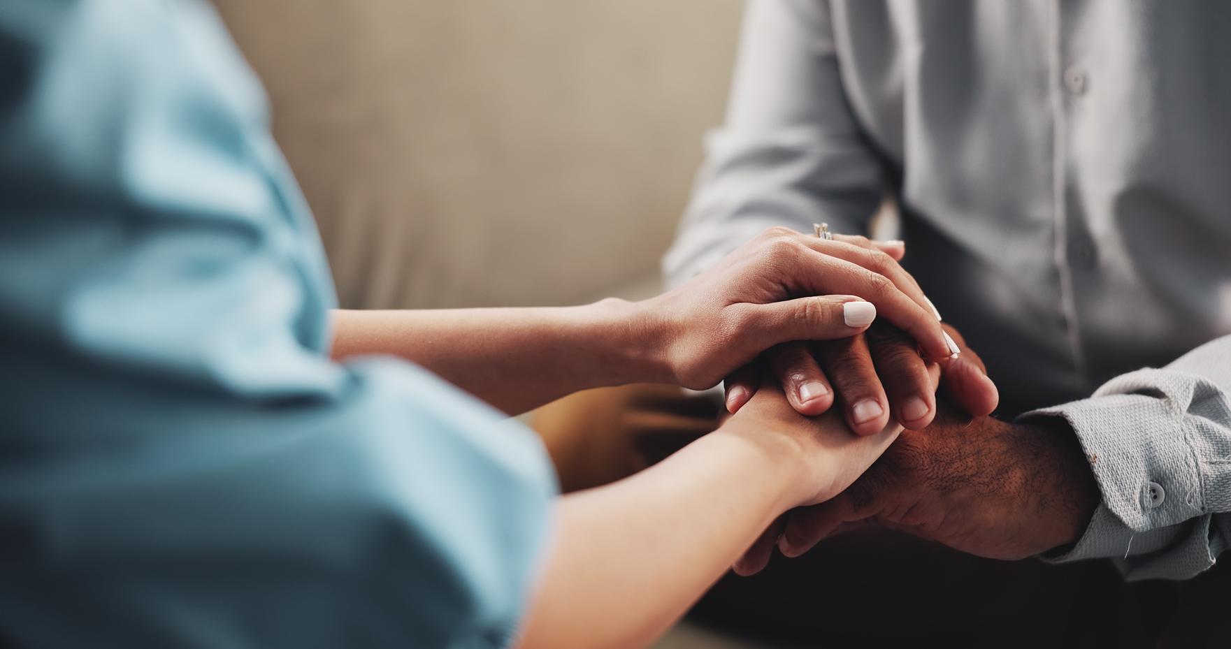 Three people place their hands together in a stack, showing unity and teamwork.